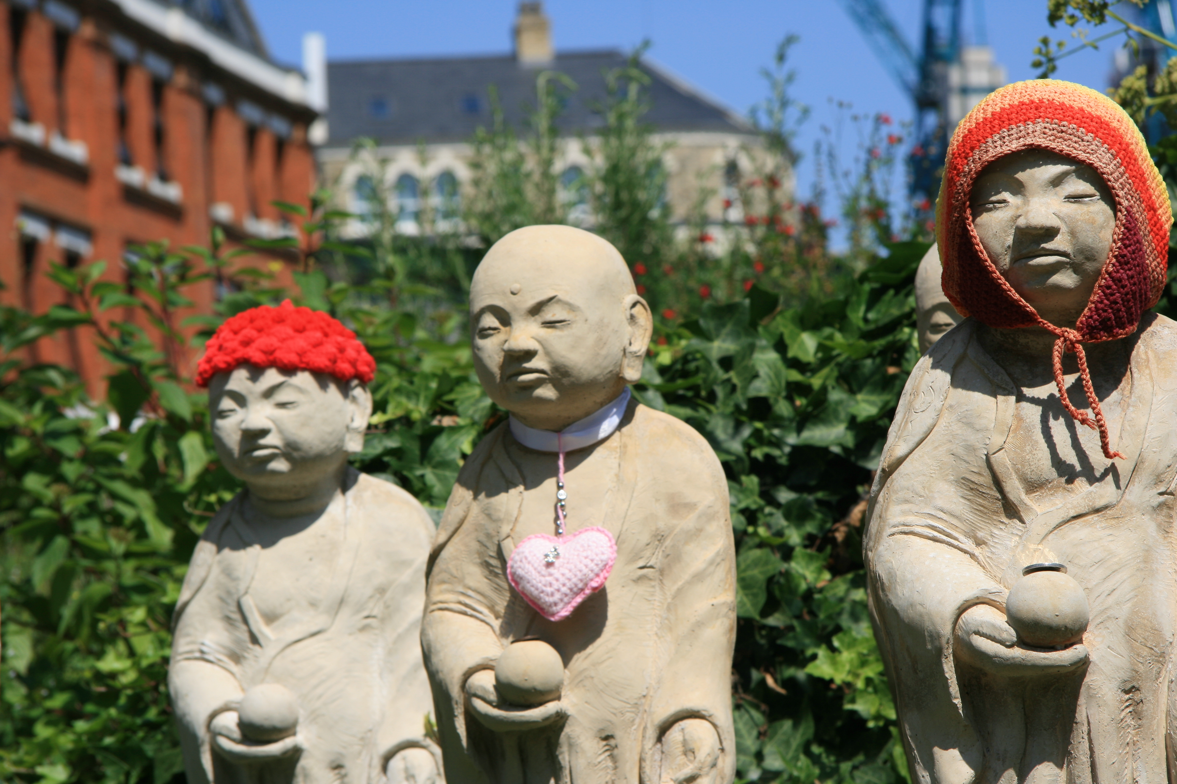 A photograph of a Mizuko Jizo statue wearing a pink heart-shaped pendant