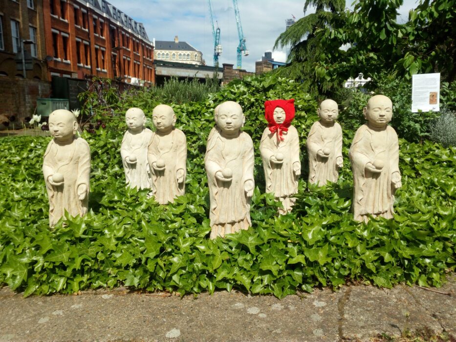 Stone Mizuko Jizo statues standing in a carpet of ivy against an urban background