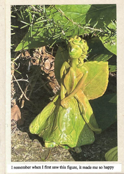 Small green fairy figurine with leaf‑like wings placed among soil and plants in sunlight. Text reads 'I remember when I saw this figure, it made me so happy'